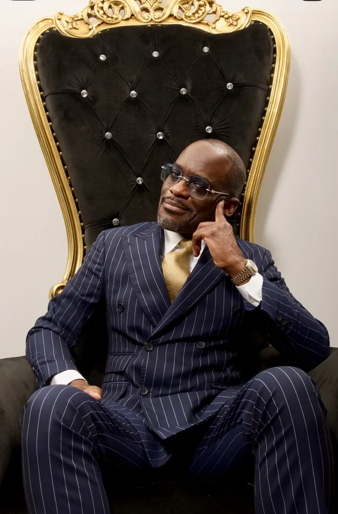 Dr. Glenn Toby on the gold throne in a navy pinstripe suit
